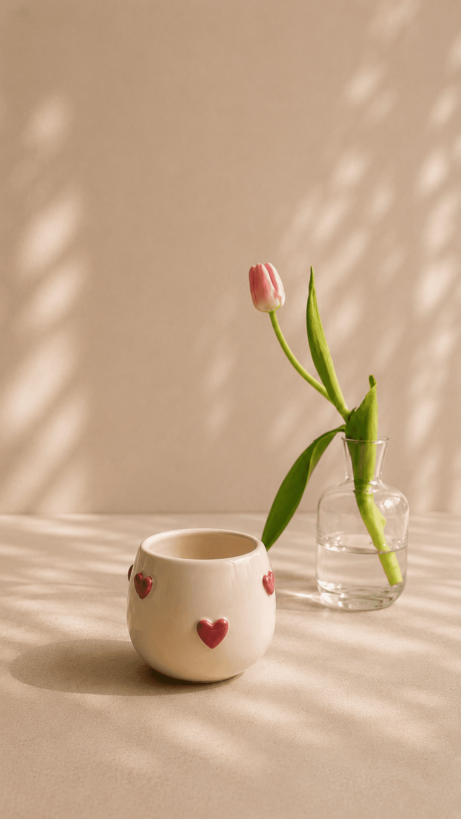 Cream cup with raised red hearts beside a tulip
